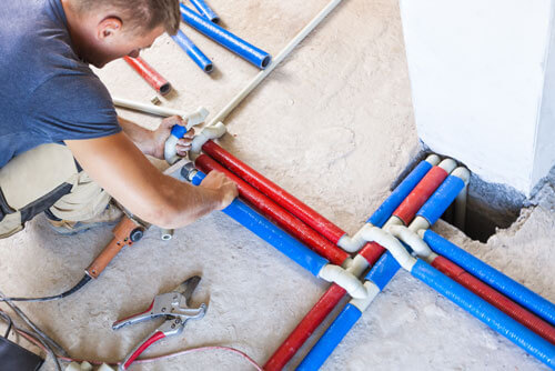 A professional plumber working on hot water system pipes.