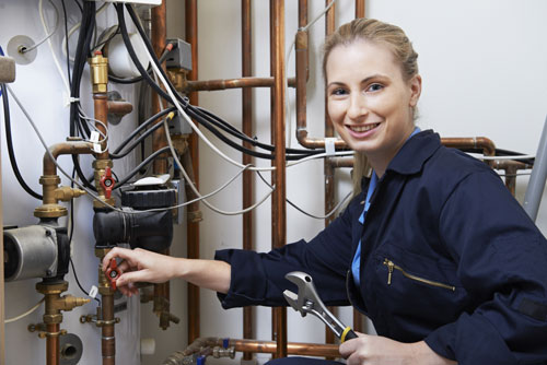 A professional plumber working her way through a complex hot water system piping.